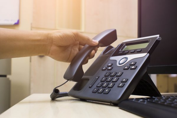 phone power voip service cost price man on voip phone in office monitor and keyboard in the background on desk